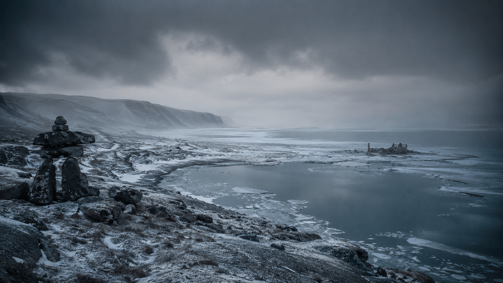 A stone inukshuk stands on a rocky, snow-dusted shore overlooking a vast, icy bay under a dark, overcast sky.