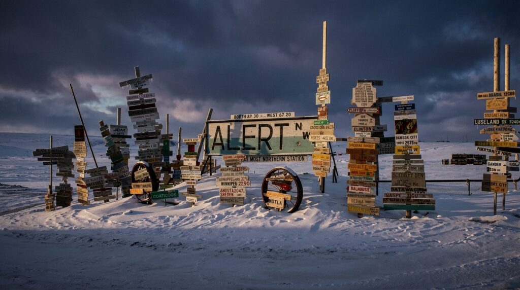 A cluster of directional signposts in a snowy, desolate landscape, featuring a central sign marked Alert, the most northern station.